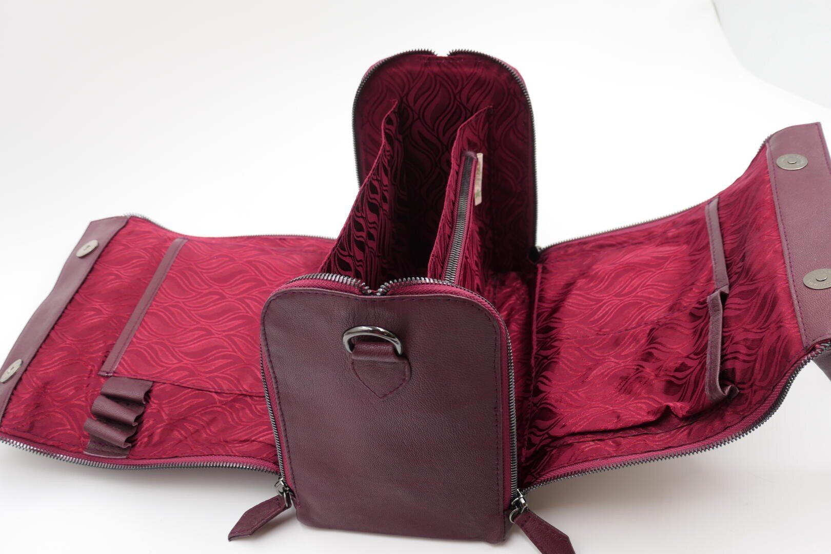 Eine kastanienbraune Ledertasche mit mehreren Fächern und Klappen, die nach dem Öffnen des Reißverschlusses ein rot gemustertes Stofffutter und organisierte Innenfächer zeigt.