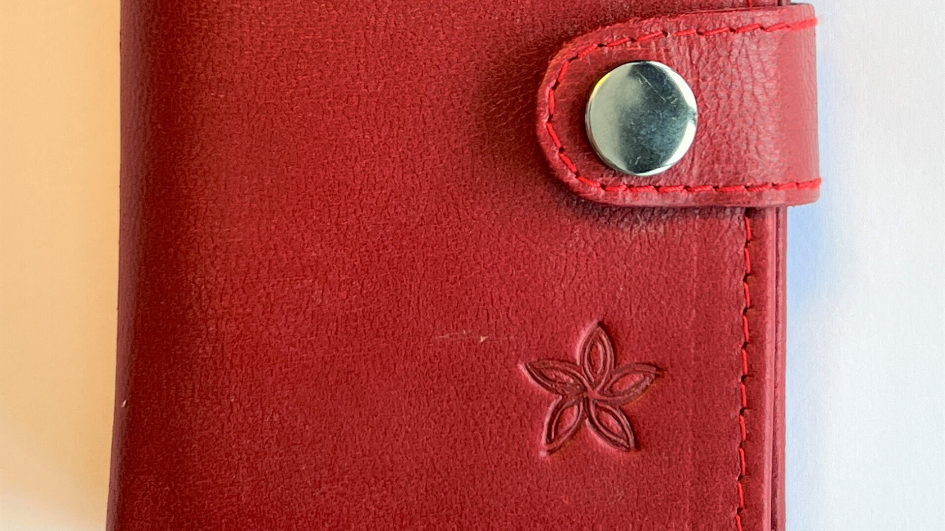 Nahaufnahme einer roten Ledergeldbörse mit einem Druckknopf aus Metall und einer blumenförmigen Prägung auf der Oberfläche.