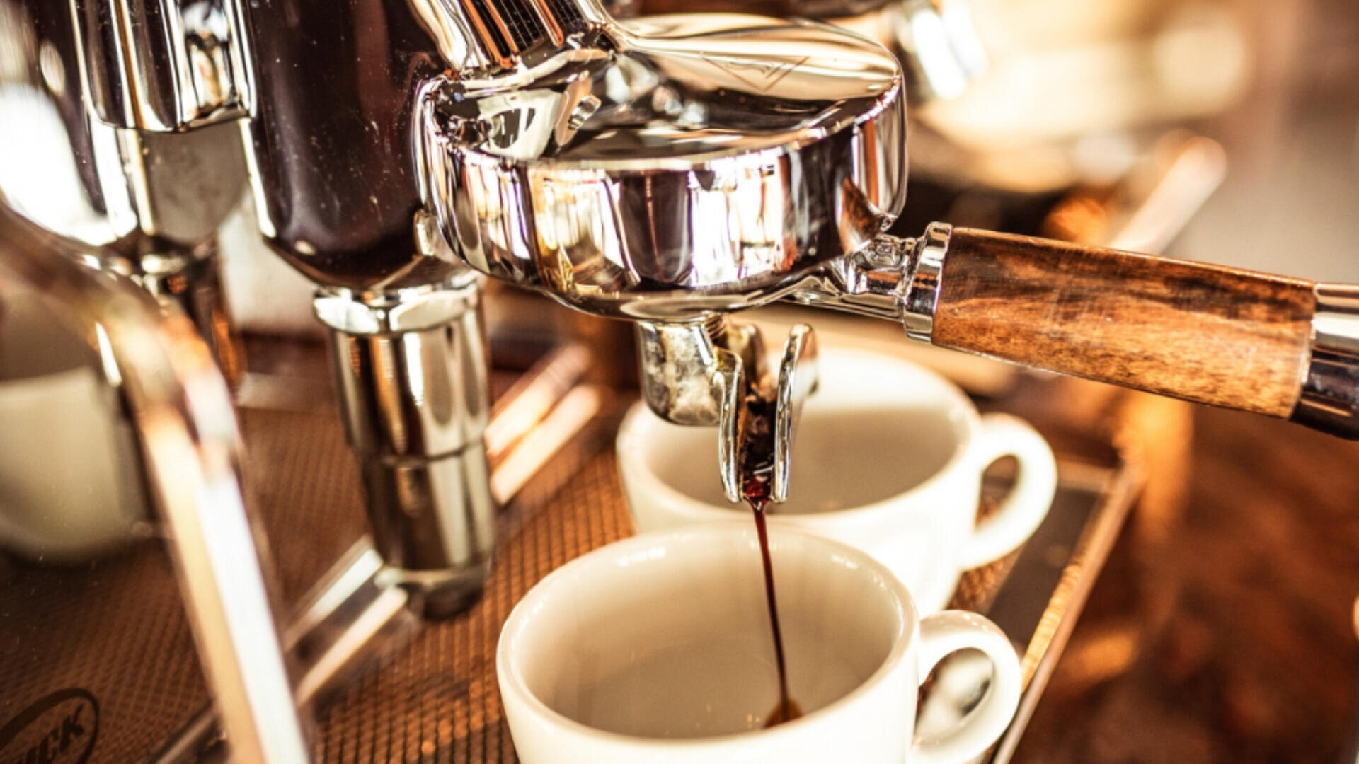 Nahaufnahme einer Espressomaschine, die Kaffee in zwei weiße Tassen ausgießt, mit einem Siebträger mit Holzgriff und einer warmen, einladenden Atmosphäre.