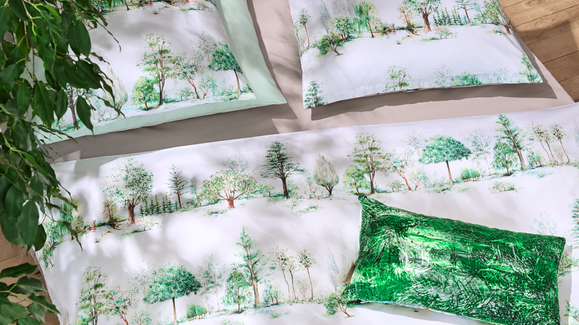 Ein Bett mit weißem und hellgrünem Bettzeug, das mit Aquarellbildern von Bäumen verziert ist. Es gibt ein leuchtend grünes Akzentkissen und eine Blattpflanze, die teilweise in der Ecke zu sehen ist. Der Boden ist aus hellem Holz.