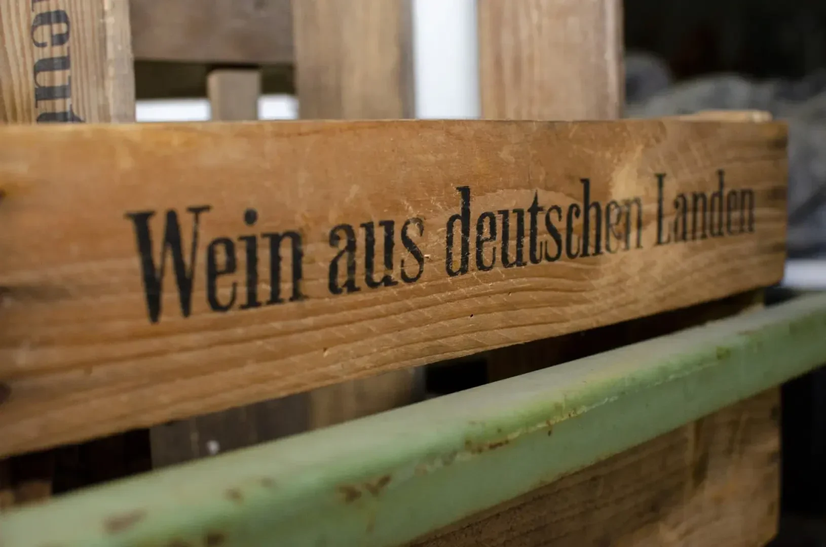 Nahaufnahme einer Holzkiste mit der Aufschrift "Wein aus deutschen Landen", die übersetzt "Wein aus deutschen Regionen" bedeutet. Die Kiste ist von anderen Holzkonstruktionen umgeben.