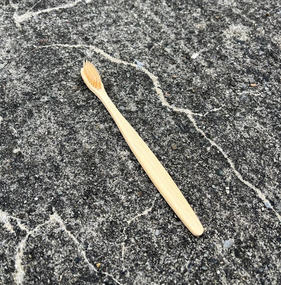 Eine Bambuszahnbürste mit hellen Borsten liegt auf einer rauen, strukturierten grauen Betonoberfläche mit sichtbaren weißen Rissen und Linien.
