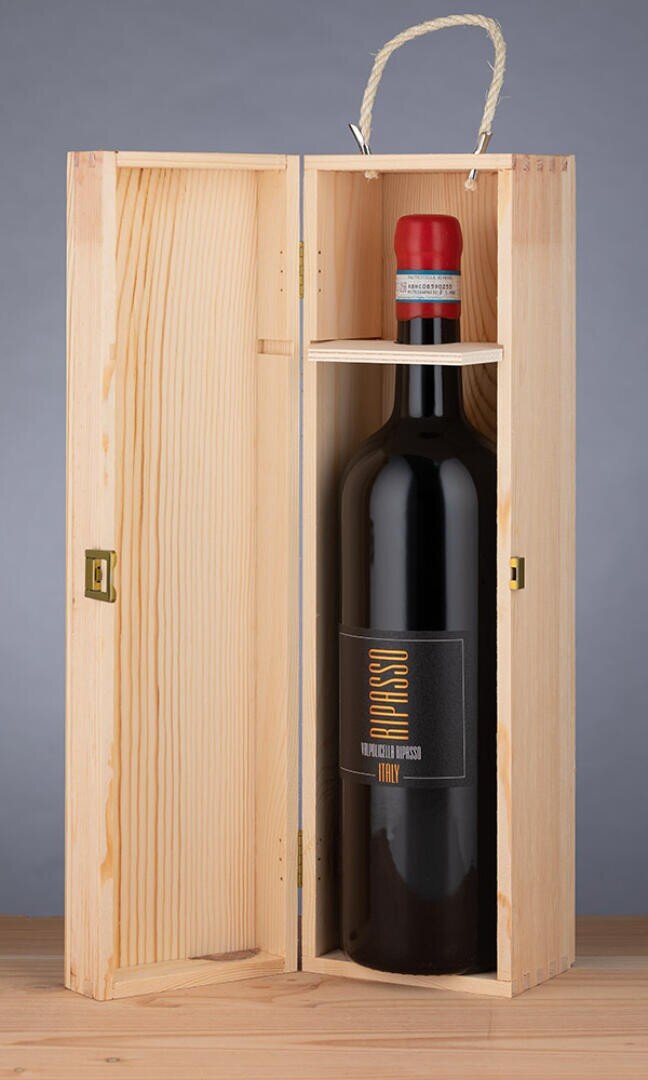 Eine Flasche italienischen Rotweins mit rotem Wachssiegel steht aufrecht in einer offenen hölzernen Geschenkbox mit einem Seilgriff, die auf einer Holzoberfläche vor einem grauen Hintergrund steht.