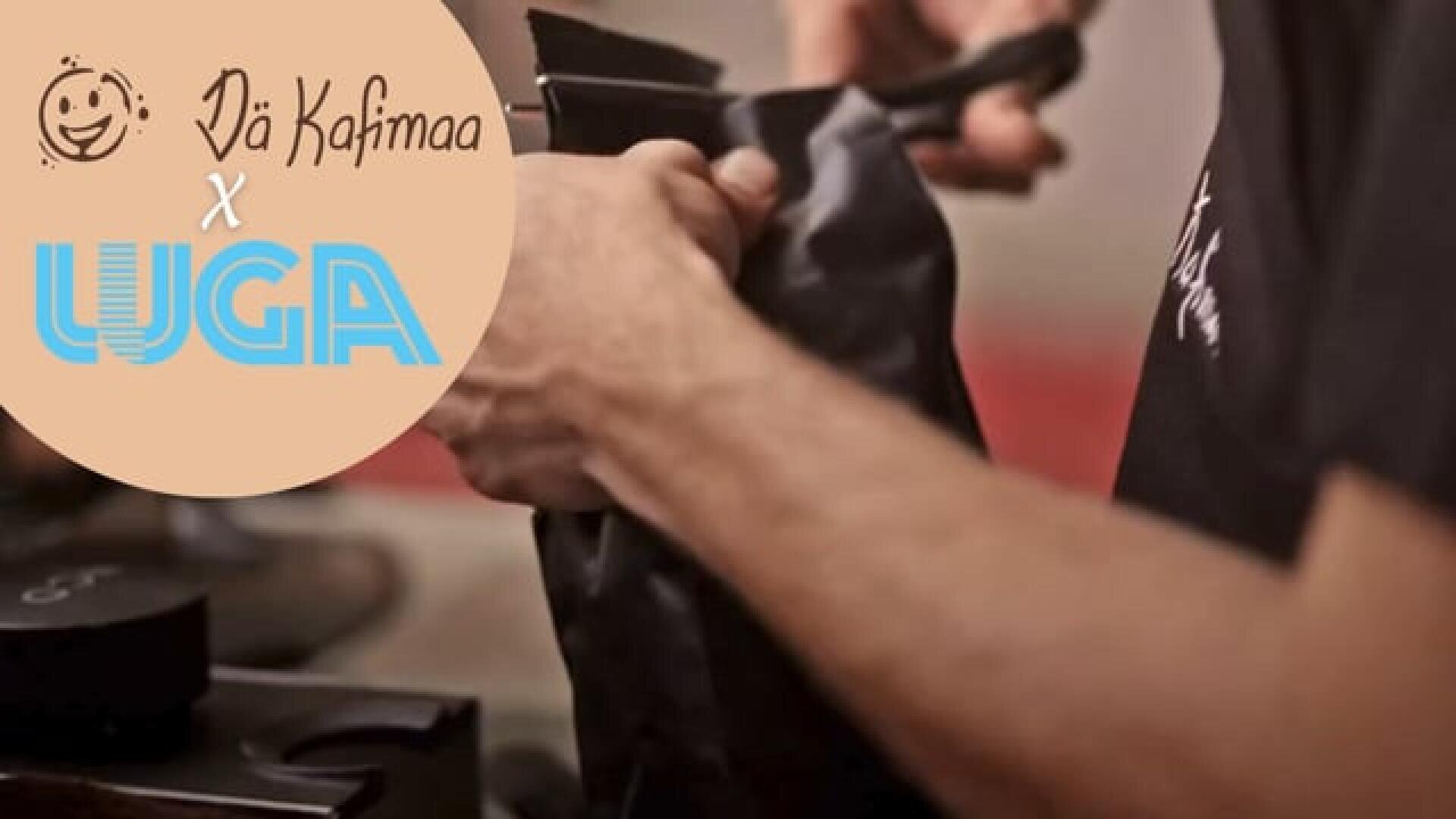 Die Hände einer Person halten eine schwarze Tüte neben einer Kaffeemühle. In der Ecke steht in einem beigen Kreis in stilisierter Schrift Dä Kahimaa x WGA.