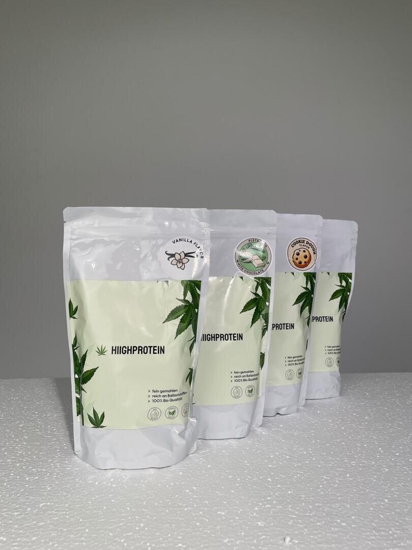 Vier Standbeutel mit HIIGHPROTEIN-Pulver in hellgrüner und weißer Verpackung mit Blattgrafik und runden Geschmacksetiketten, die auf einer weißen Fläche vor einem einfarbig grauen Hintergrund präsentiert werden.