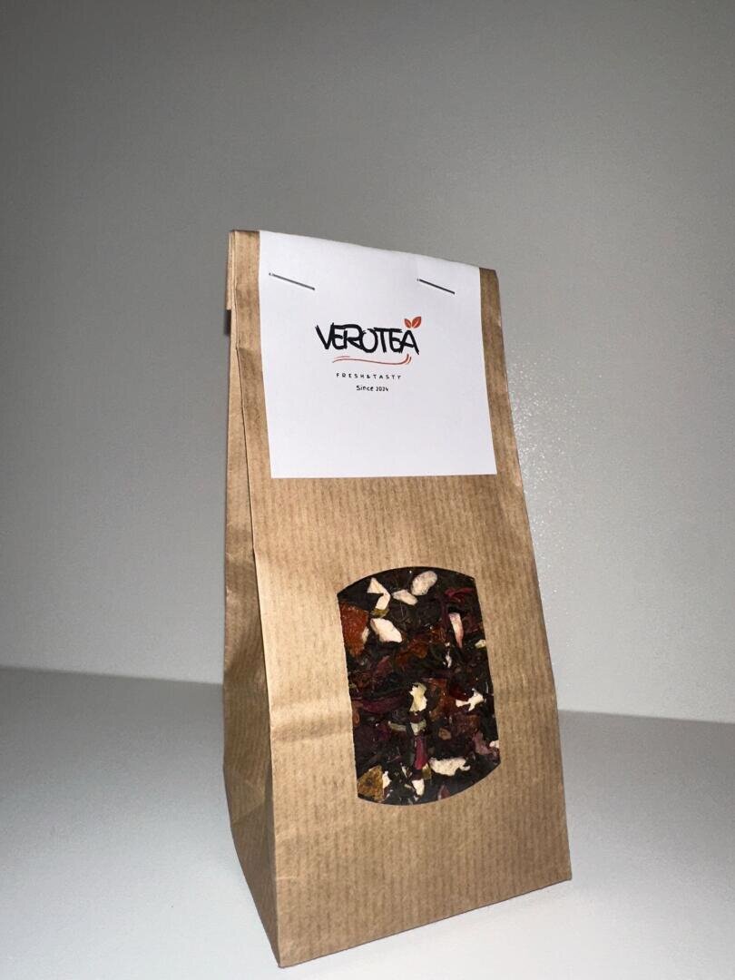 Eine braune Papiertüte mit einer Kräuterteemischung von Verotea mit einem transparenten Fenster, auf dem getrocknete Früchte und Kräuter zu sehen sind, vor einem schlichten weißen Hintergrund. Die Tüte hat ein weißes Etikett mit dem Verotea-Logo an der Oberseite.