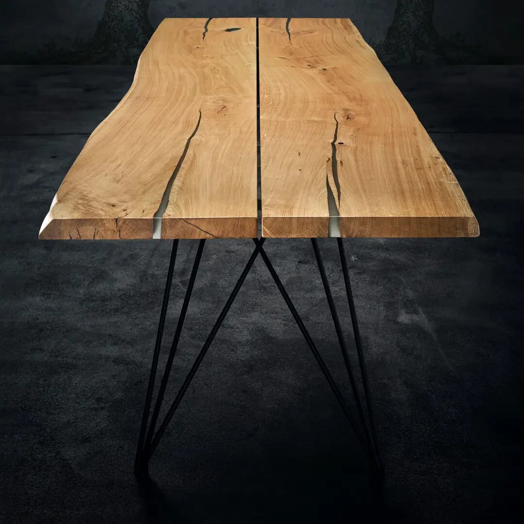 Ein Holztisch mit natürlicher, lebendiger Kante, in der Mitte geteilt, mit Metallbeinen mit geometrischem Muster, platziert auf einem dunklen Boden mit einem dezenten Baumhintergrund.